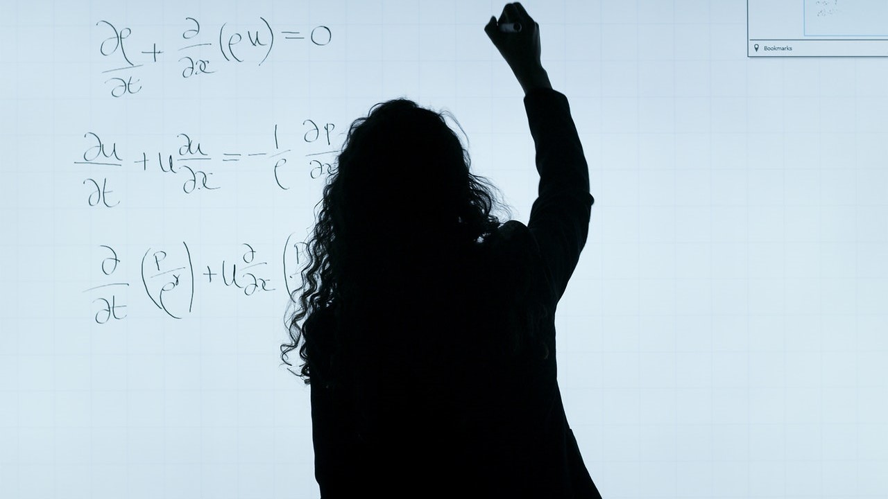A silhouette of a curly haired figure, writing equations on a white board